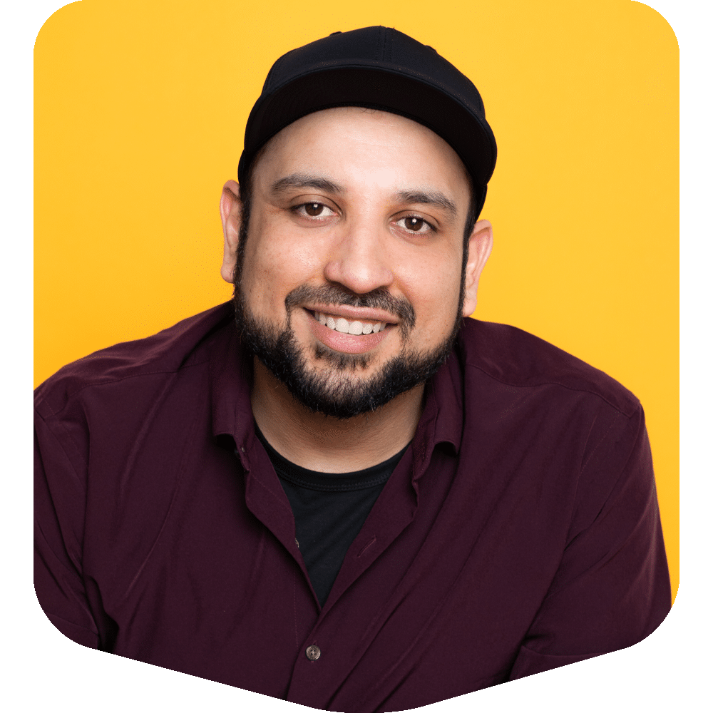 Oscar Mata, smiling warmly in a burgundy button-down and black cap, against a bold yellow backdrop.