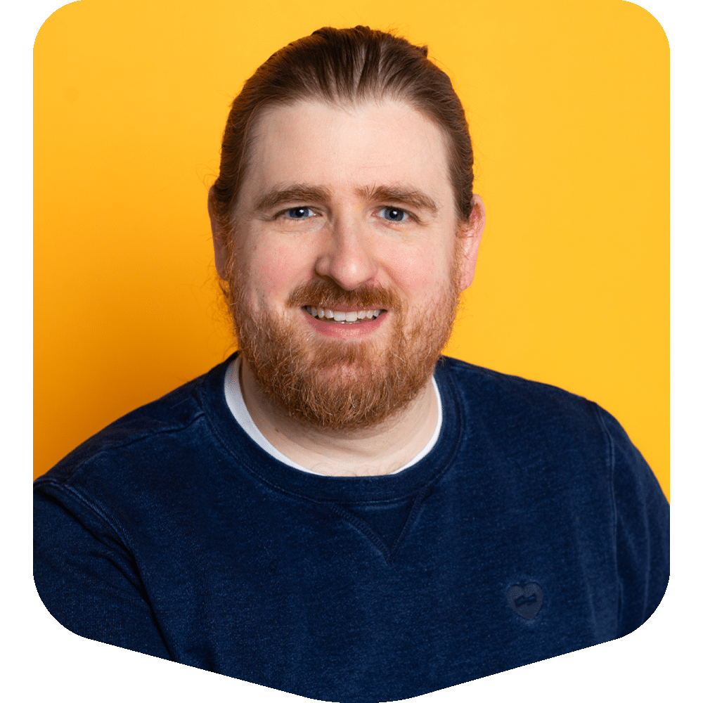 Scott Conor, smiling in a navy blue sweatshirt against a bold yellow background.